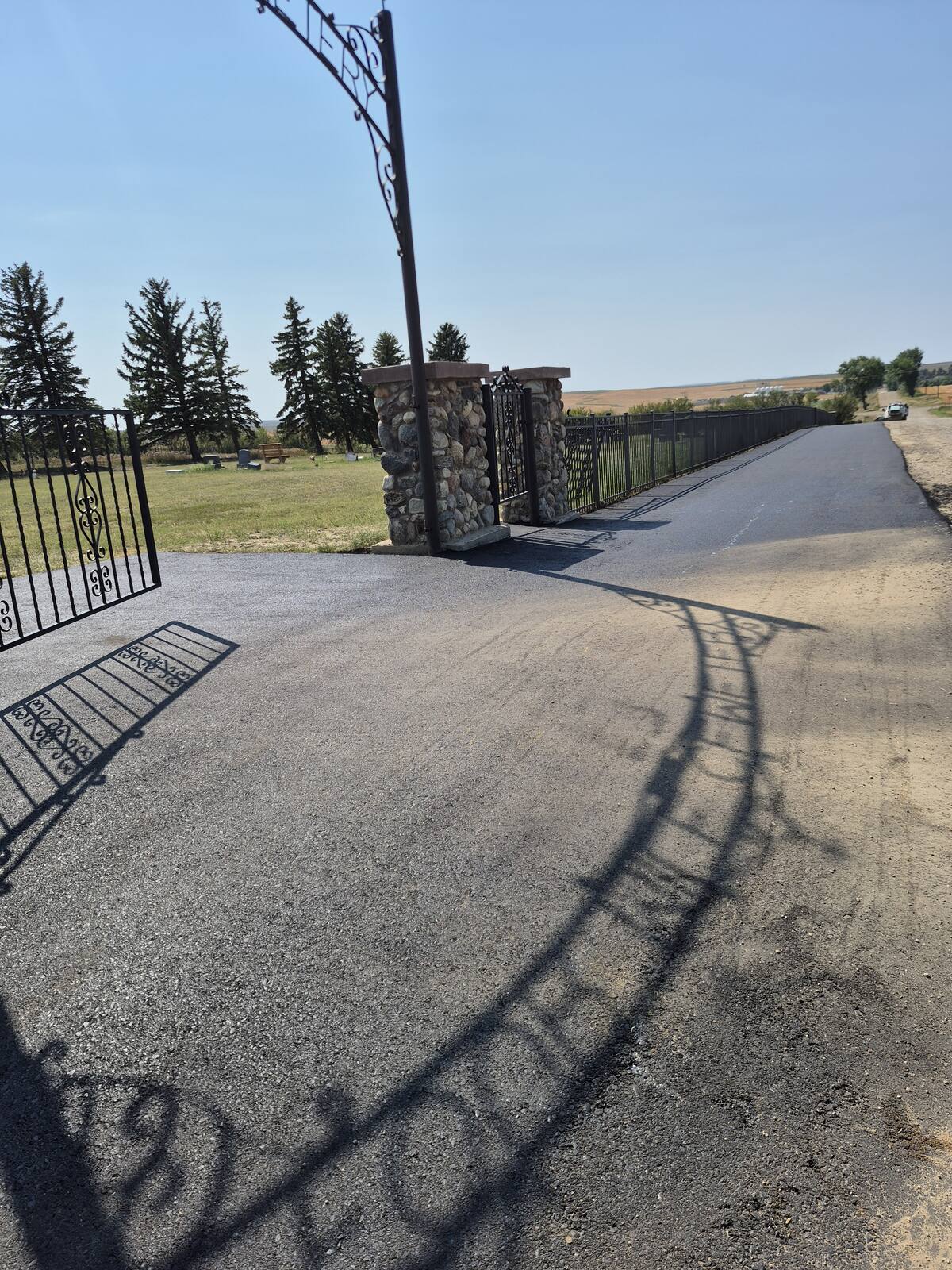 New asphalt at the Four Mile Cemetery gate with the shadow of the entrance arch across it