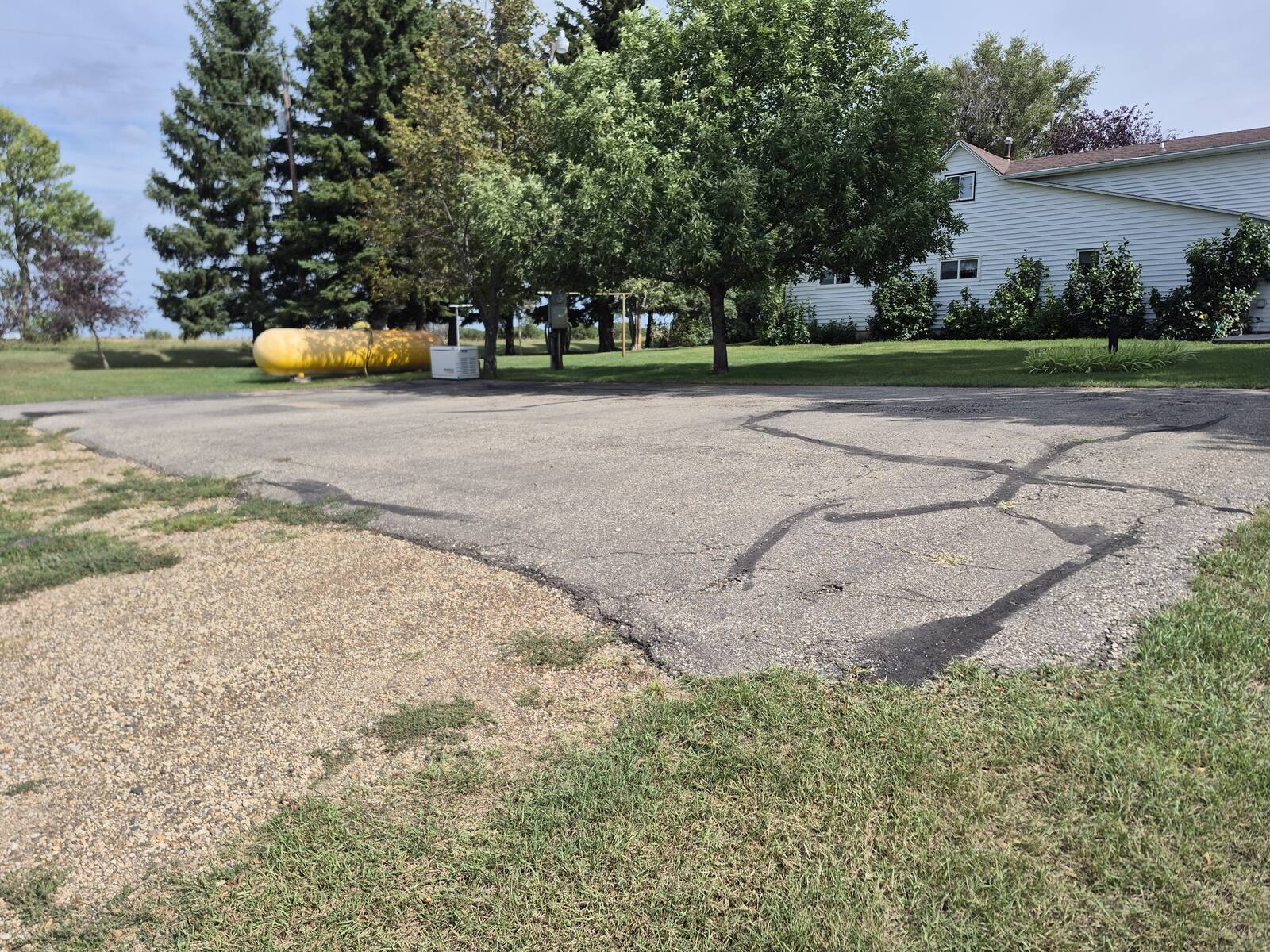 Cracked and faded asphalt parking pad beside a house before the overlay