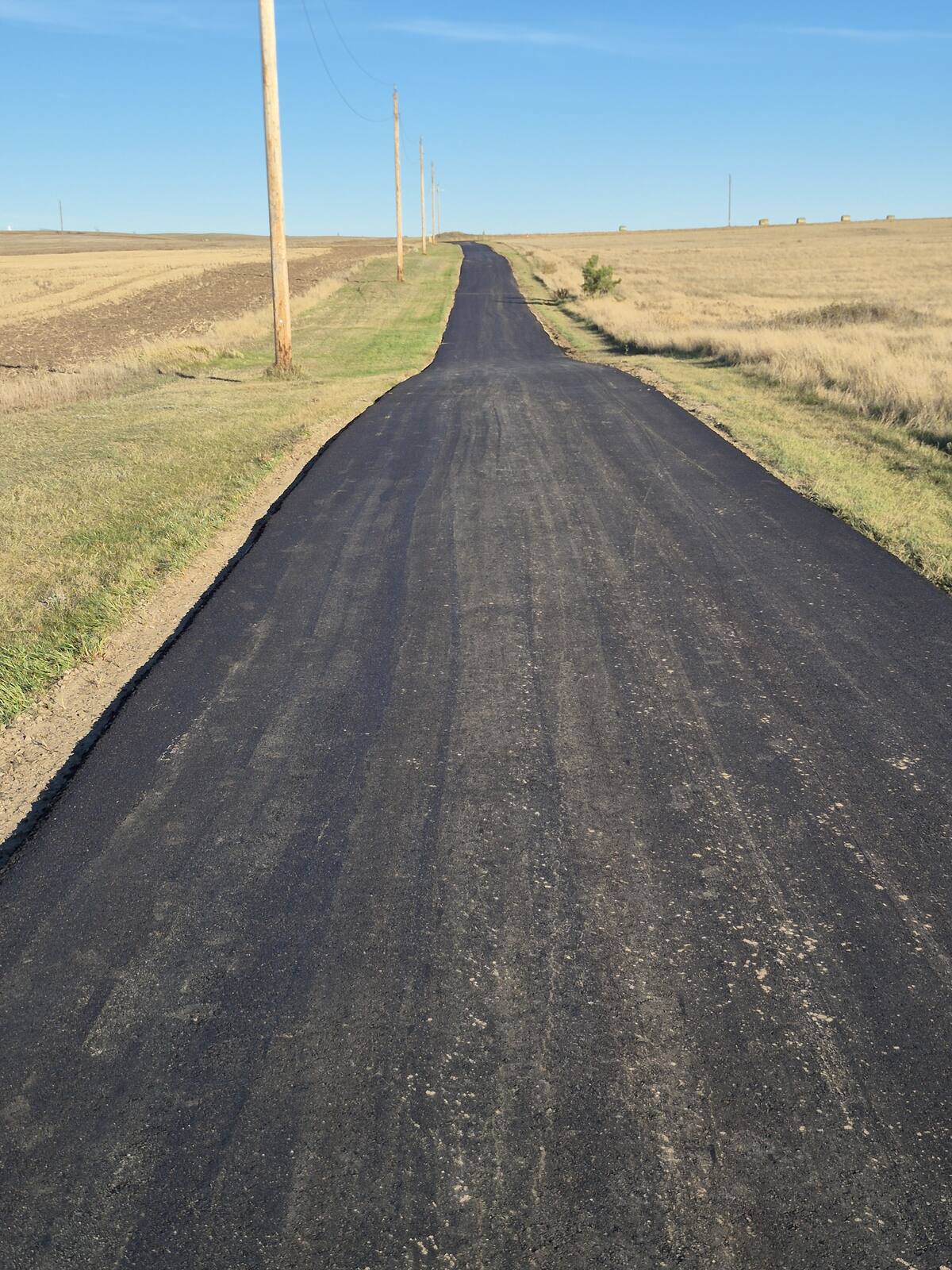 Long new asphalt driveway running toward the horizon between fields