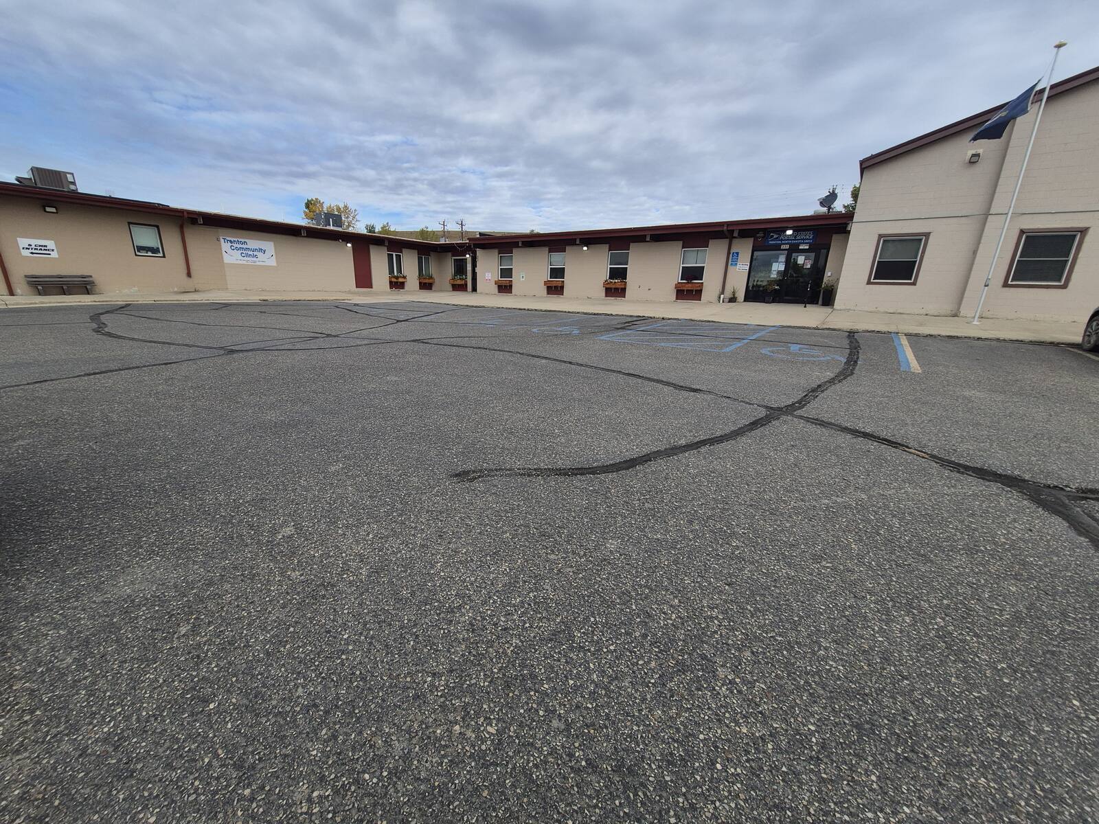 Cracked parking lot with faded striping in front of a long single-story building before the overlay