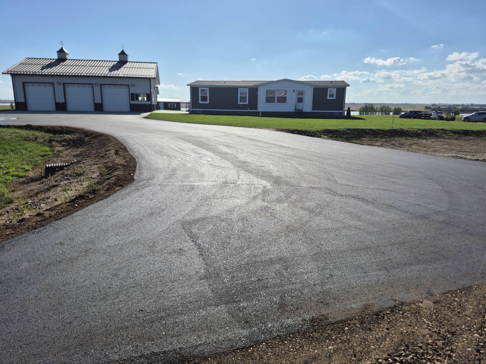 Wide new asphalt driveway in front of a shop and home